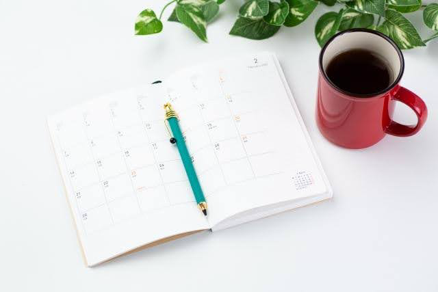 カレンダーとペン、コーヒーカップが並ぶデスク。アートメイク2回目の施術タイミングを考えるイメージ写真