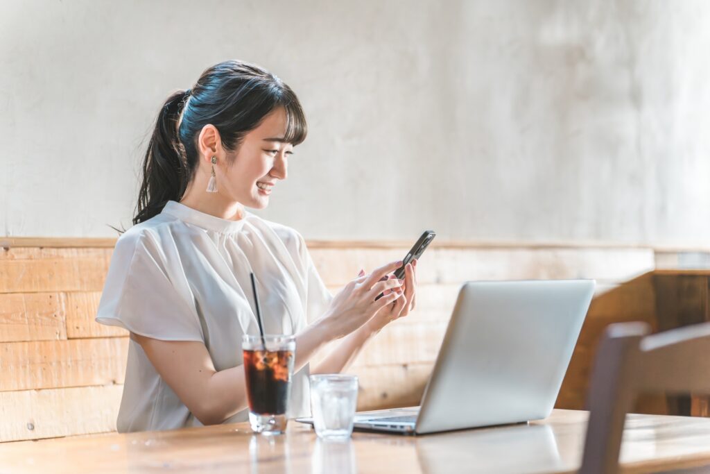 カフェでスマホとノートPCを見る女性（働き方を考えるイメージ）